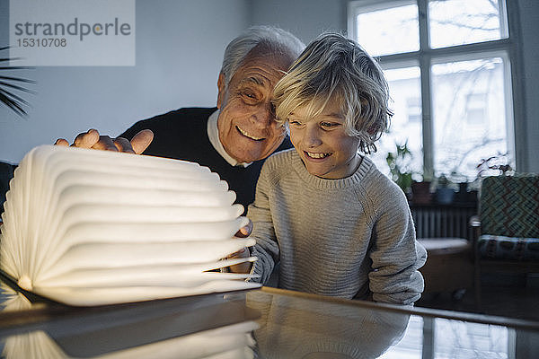 Glücklicher Großvater und Enkel schauen zu Hause auf leuchtendes Buch