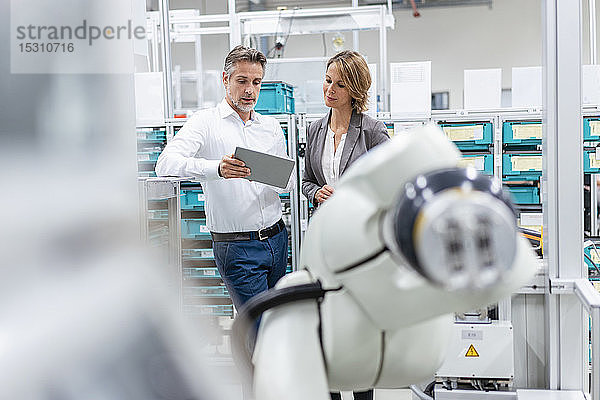 Geschäftsfrau und Mann mit Tablette sprechen am Montageroboter in einer Fabrik