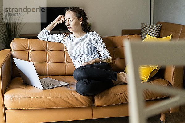 Junge Frau sitzt zu Hause auf der Couch mit Laptop
