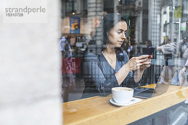 Geschäftsfrau  die in einem Café eine Pause macht und mit Laptop und Smartphone arbeitet