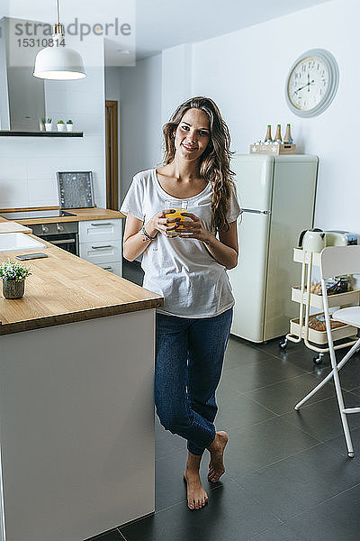 Porträt einer lächelnden jungen Frau  die in der Küche Orangensaft trinkt