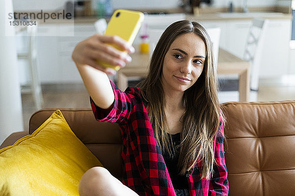 Junge Frau  die zu Hause auf einer Couch ein Selfie macht