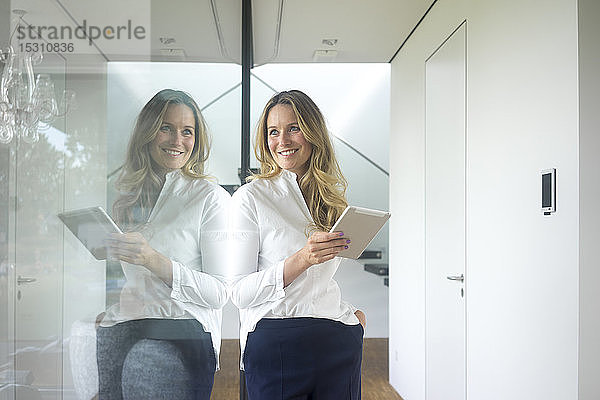 Lächelnde Geschäftsfrau hält Tablette in modernem Haus