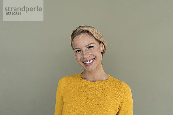 Porträt einer lächelnden blonden Frau  die einen gelben Pullover trägt