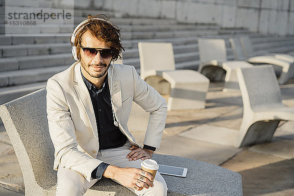 Porträt eines Geschäftsmannes mit Sonnenbrille  der mit Kopfhörern Musik hört
