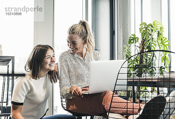 Zwei fröhliche lockere Geschäftsfrauen mit Laptop treffen sich im Büro