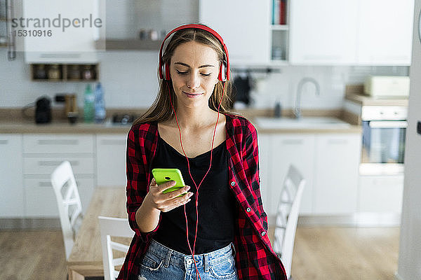 Junge Frau mit Handy und Kopfhörern zu Hause