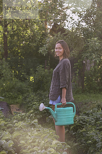 Lächelnde junge Frau mit Gießkanne im Garten