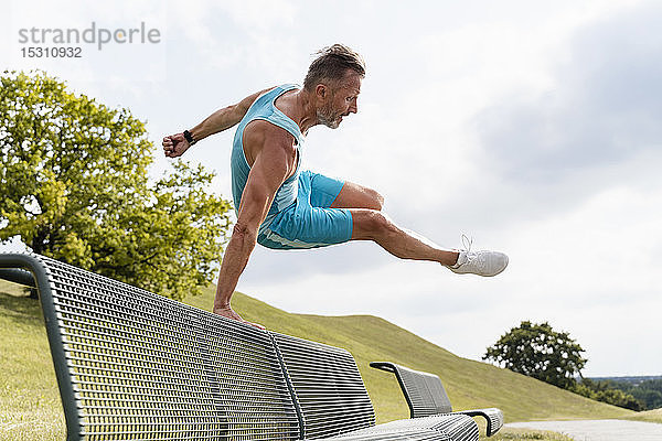 Sportlicher Mann springt in einem Park über eine Bank