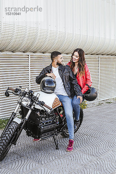 Glückliches Paar mit Motorradhelmen auf Motorrad sitzend