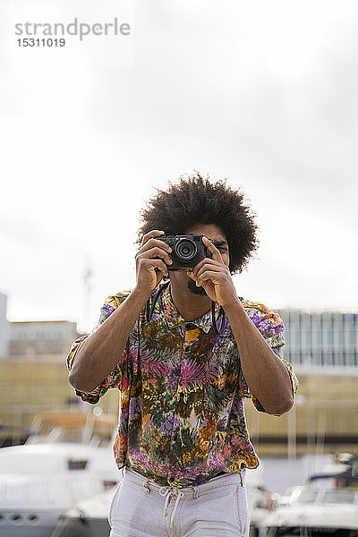 Mann mit farbigem Hemd fotografiert mit einer Kamera