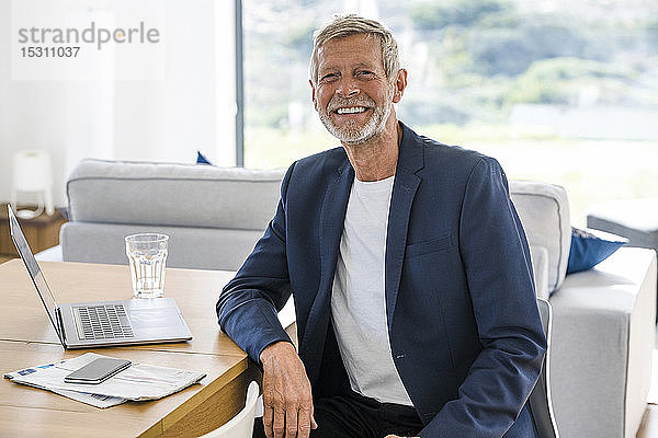 Porträt eines lächelnden älteren Geschäftsmannes mit Laptop  der zu Hause am Schreibtisch sitzt