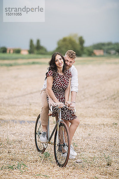 Portrait eines Paares auf einem handgefertigten Rennrad auf Stoppelfeld