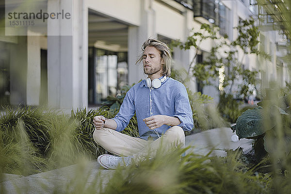 Junger Mann meditiert vor Bürogebäude