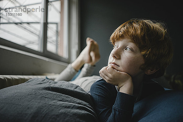 Porträt eines rothaarigen Jungen  der auf einer Couch aus dem Fenster liegt