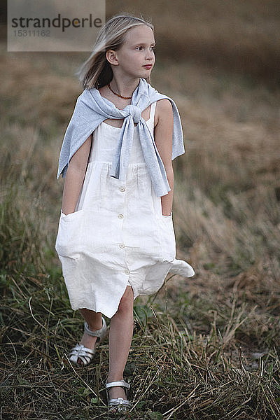 Bildnis eines blonden kleinen Mädchens in weißem Sommerkleid  das auf einer Wiese spazieren geht