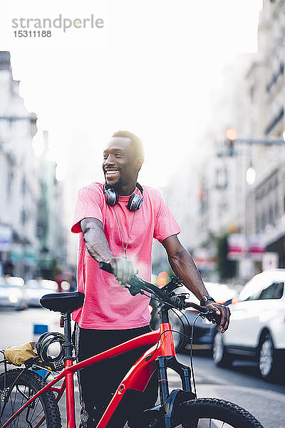 Lächelnder junger Mann mit E-Fahrrad in der Stadt