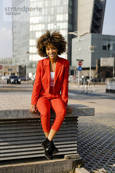 Porträt einer lächelnden jungen Frau in einem modischen roten Hosenanzug in der Stadt