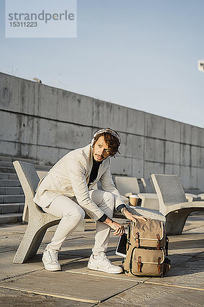 Porträt eines Geschäftsmannes mit Kopfhörern  der ein digitales Tablet aus dem Kofferraum nimmt