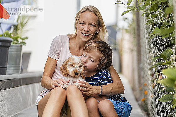 Porträt von Mutter und Sohn beim Kuscheln mit süßem Hundewelpen
