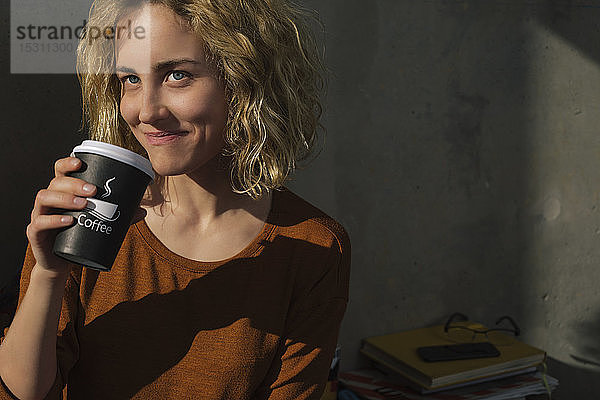 Porträt einer lächelnden jungen Frau  die Kaffee trinkt  um nach Hause zu gehen