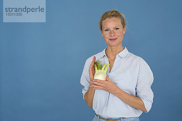 Lächelnde blonde Frau mit Fenchel  blauer Hintergrund