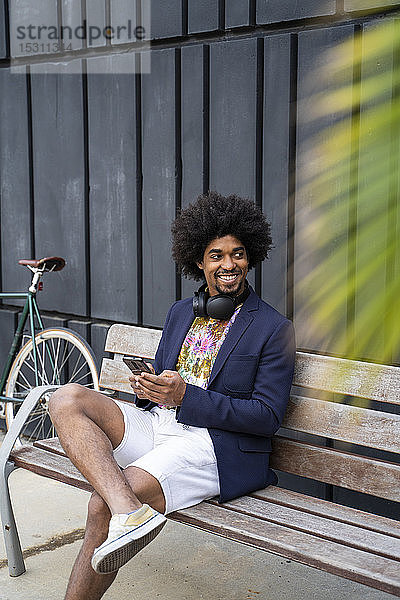 Lächelnder stilvoller Mann mit Handy auf einer Bank sitzend