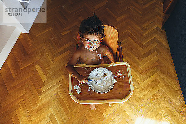Kleiner Junge frühstückt zu Hause  im Hochstuhl sitzend  von oben
