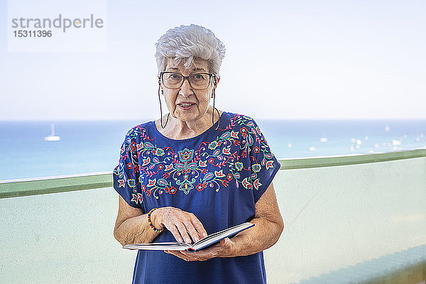 Ältere Frau liest ein Buch auf einer Terrasse