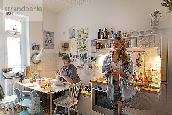 Junge Frau in Yoga-Pose in häuslicher Küche mit Partner im Hintergrund