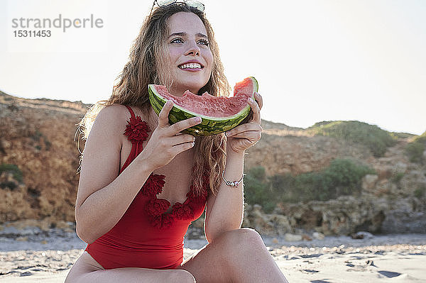 Glückliche junge Frau hält Wassermelonenscheibe am Strand