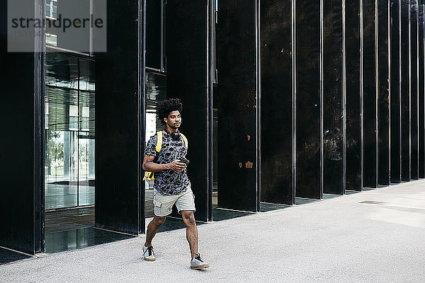 Mann mit gelbem Rucksack  Smartphone und Kopfhörern geht die Straße entlang  Barcelona  Spanien