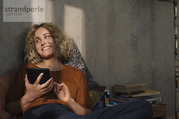 Porträt einer glücklichen jungen Frau  die mit einem E-Book-Reader auf dem Bett liegt