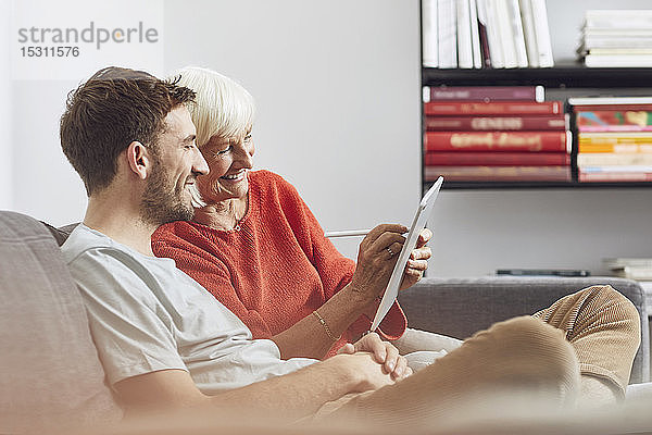 Enkel sitzt auf der Couch und benutzt mit seiner Großmutter ein digitales Tablet