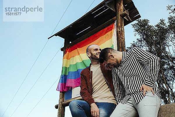 Glückliches schwules Paar mit der Gay-Pride-Flagge auf einer Reise