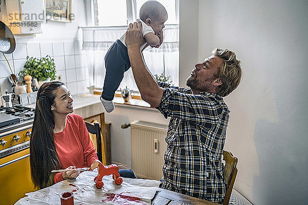 Familie hebt Baby am Küchentisch zu Hause hoch