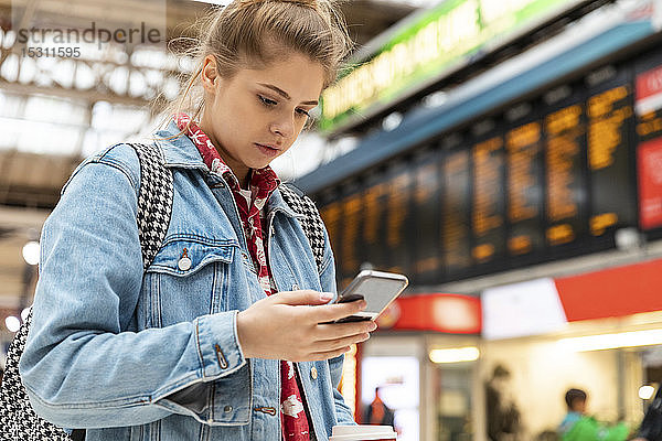 Junge Frau überprüft Smartphone am Bahnhof