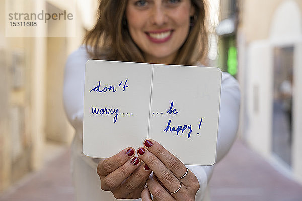 Porträt einer lächelnden Frau  die ein Notizbuch hält: Mach dir keine Sorgen  sei glücklich!