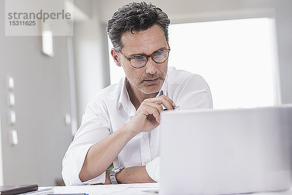 Geschäftsmann  der in einem hellen Büro arbeitet und einen Laptop benutzt