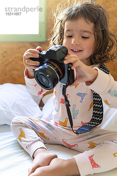 Süßes kleines Mädchen im Pyjama im Bett mit einer Kamera
