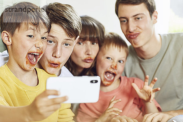Mutter und ihre vier Söhne mit Smartphone-Selbstfahrern beim Mittagessen  mit Gesichtern voller Tomatensauce