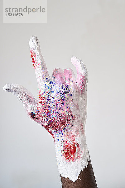 Künstlerhand mit farbenfroher Farbe bedeckt  während sie das Zeichen der Hörner macht