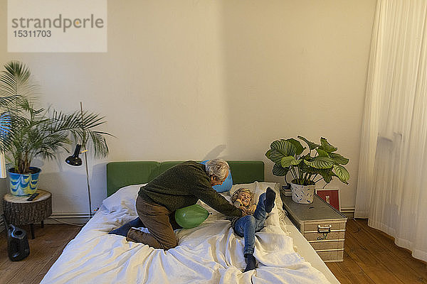Glücklicher Großvater spielt mit seinem Enkel zu Hause im Bett