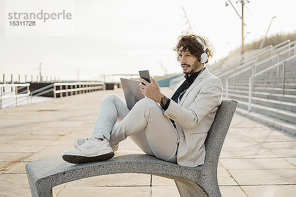 Porträt eines schockierten Geschäftsmannes mit Kopfhörer und Laptop  der auf sein Mobiltelefon schaut