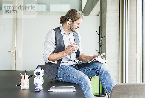 Junger Geschäftsmann sitzt im Büro mit Tablette und Tasse Kaffee auf dem Tisch