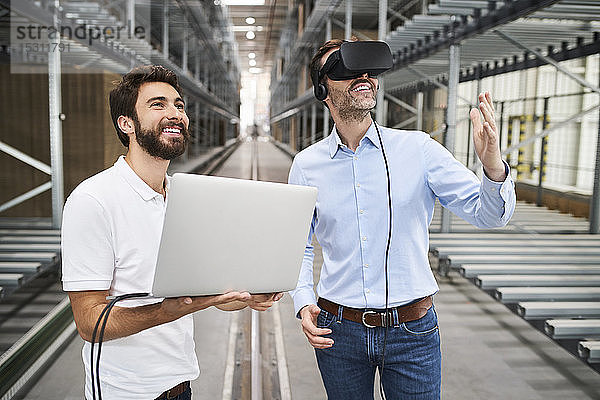 Mann mit Laptop und Geschäftsmann mit VR-Brille in der Fabrik
