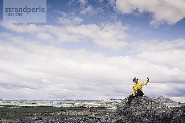 Junge Frau sitzt auf einem Felsen in Myvatn  Island  und nimmt sich