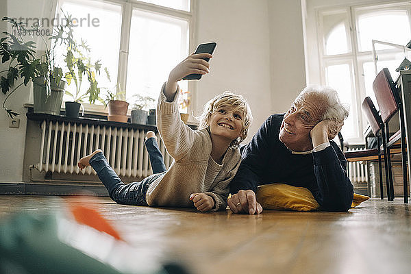 Großvater und Enkel liegen zu Hause auf dem Boden und machen ein Selfie