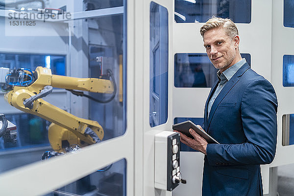 Porträt eines selbstbewussten Geschäftsmannes vor einem Roboter in einer modernen Fabrik