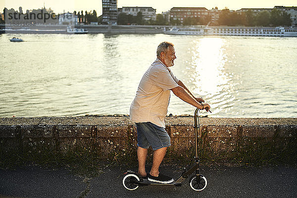 Älterer Mann fährt E-Scooter am Flussufer